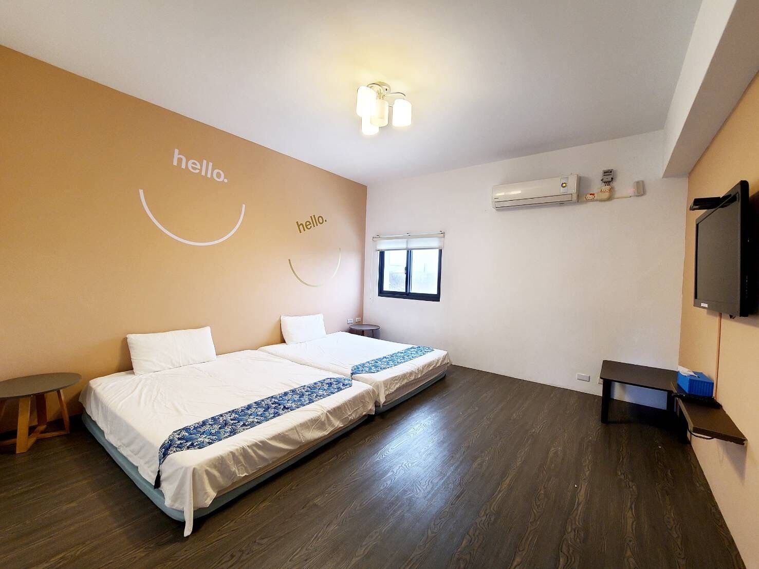 A hotel room with two beds, a small table, a TV, and a window.