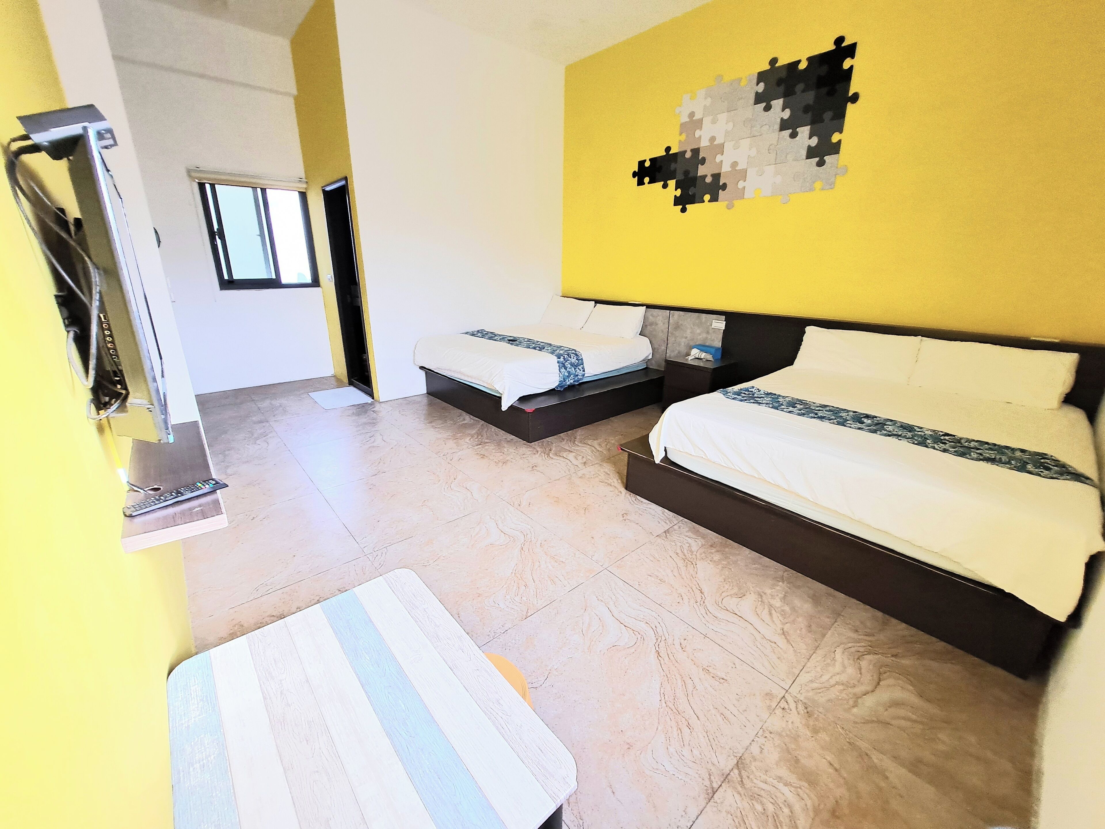 A hotel room with two beds, a small table, and a wall-mounted TV.
