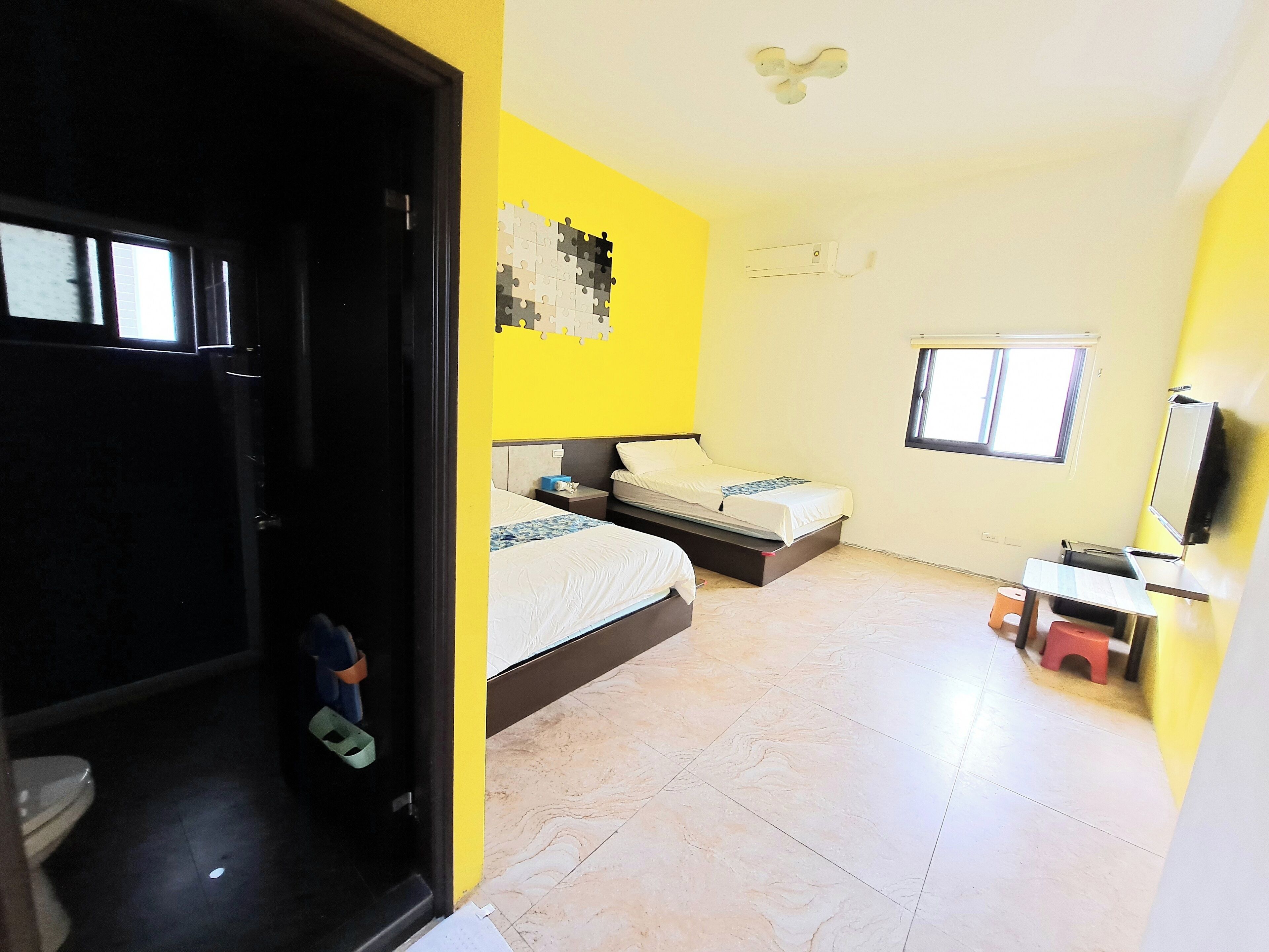 A room with two beds, a window, a TV, and a small stool.