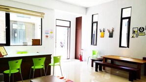 Un moderno vestíbulo de hotel con una recepción, sillas verdes, un banco de madera y un ventanal grande.