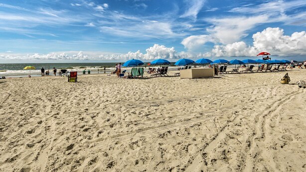 A beach with blue umbrellas, a lifeguard tower, and beach chairs. - Relax by Pool & Walk to Beach: Hilton Head Condo! (Hilton Head Island)