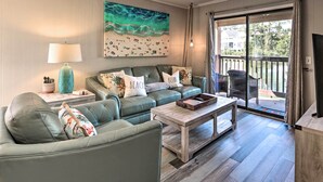A living room with a green sofa, a wooden coffee table, and a painting of a beach scene. - Relax by Pool & Walk to Beach: Hilton Head Condo! (Hilton Head Island)
