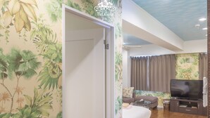 Ein Zimmer mit einem Bett, einem Fernseher und einer Wand mit tropischem Wandpapier.