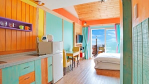 Quarto compacto com cozinha compacta, cama, escrivaninha e janela com cortinas.