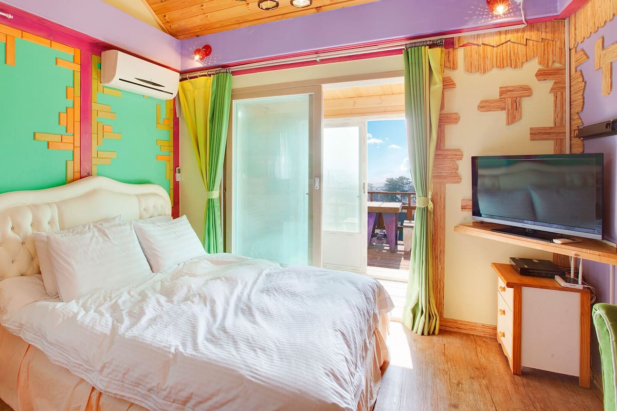 A bedroom with a bed, a television, and a window with curtains.