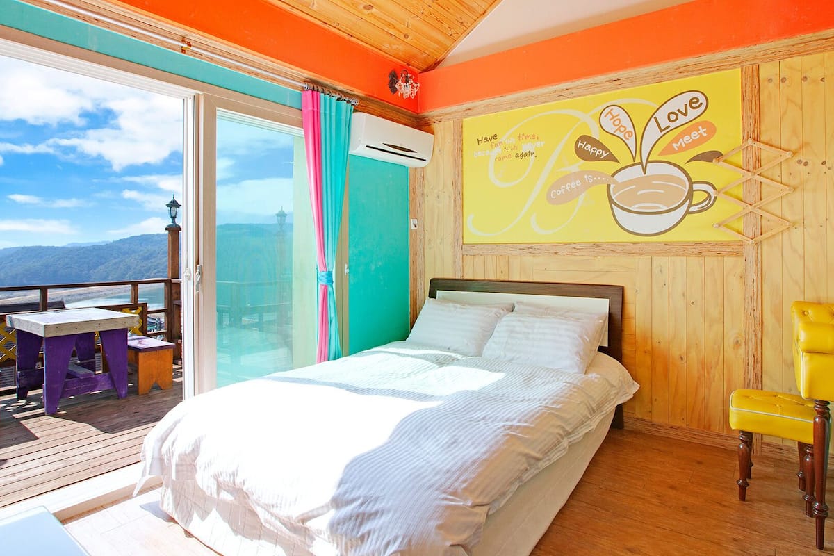A bedroom with a bed, a yellow chair, and a mural on the wall.