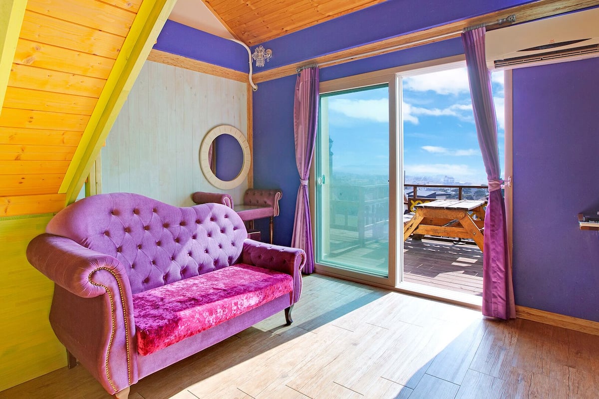 A room with a purple sofa, wooden flooring, and a large sliding glass door leading to an outdoor deck.