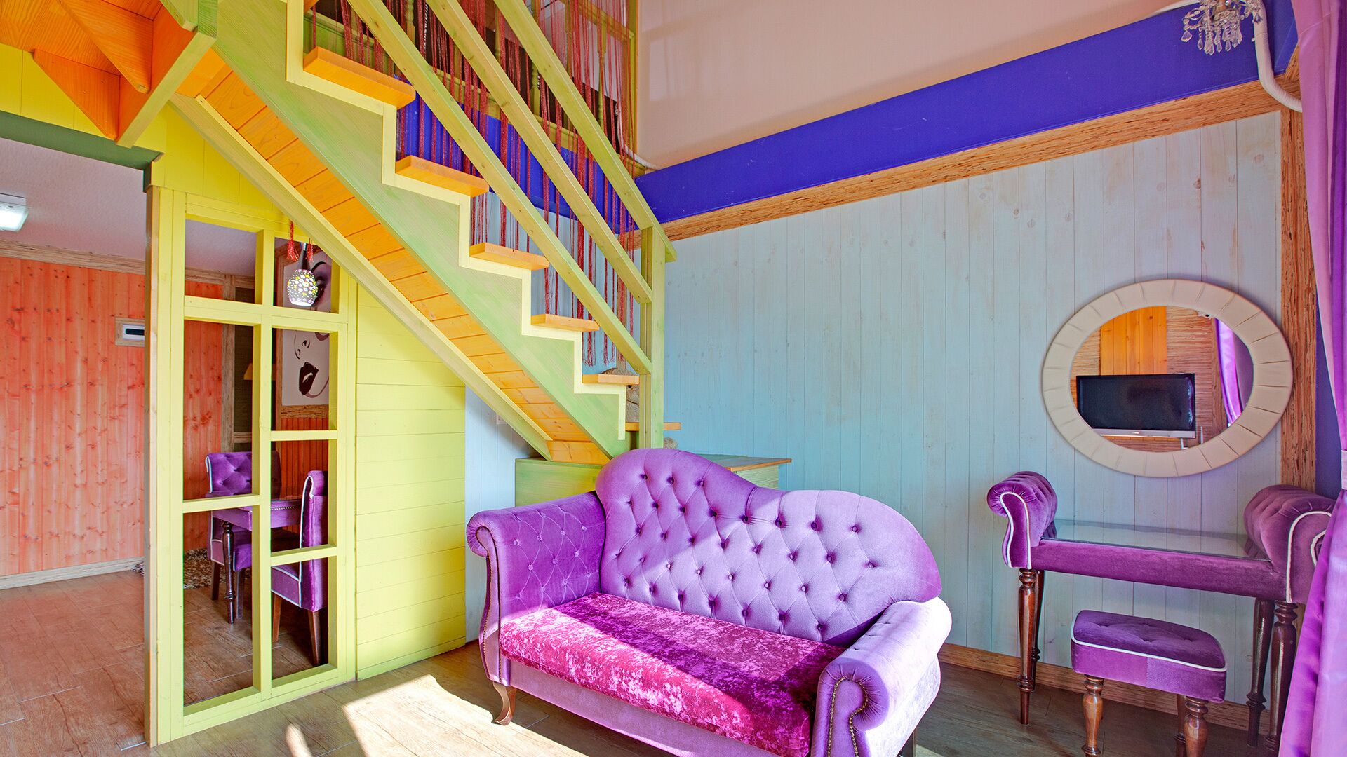 Ein Zimmer mit einem violetten Sofa, einer Holztreppe und einem Spiegel an der Wand.