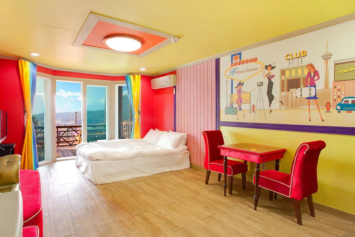 A room with a bed, a table, and chairs, a television, and a mural on the wall.