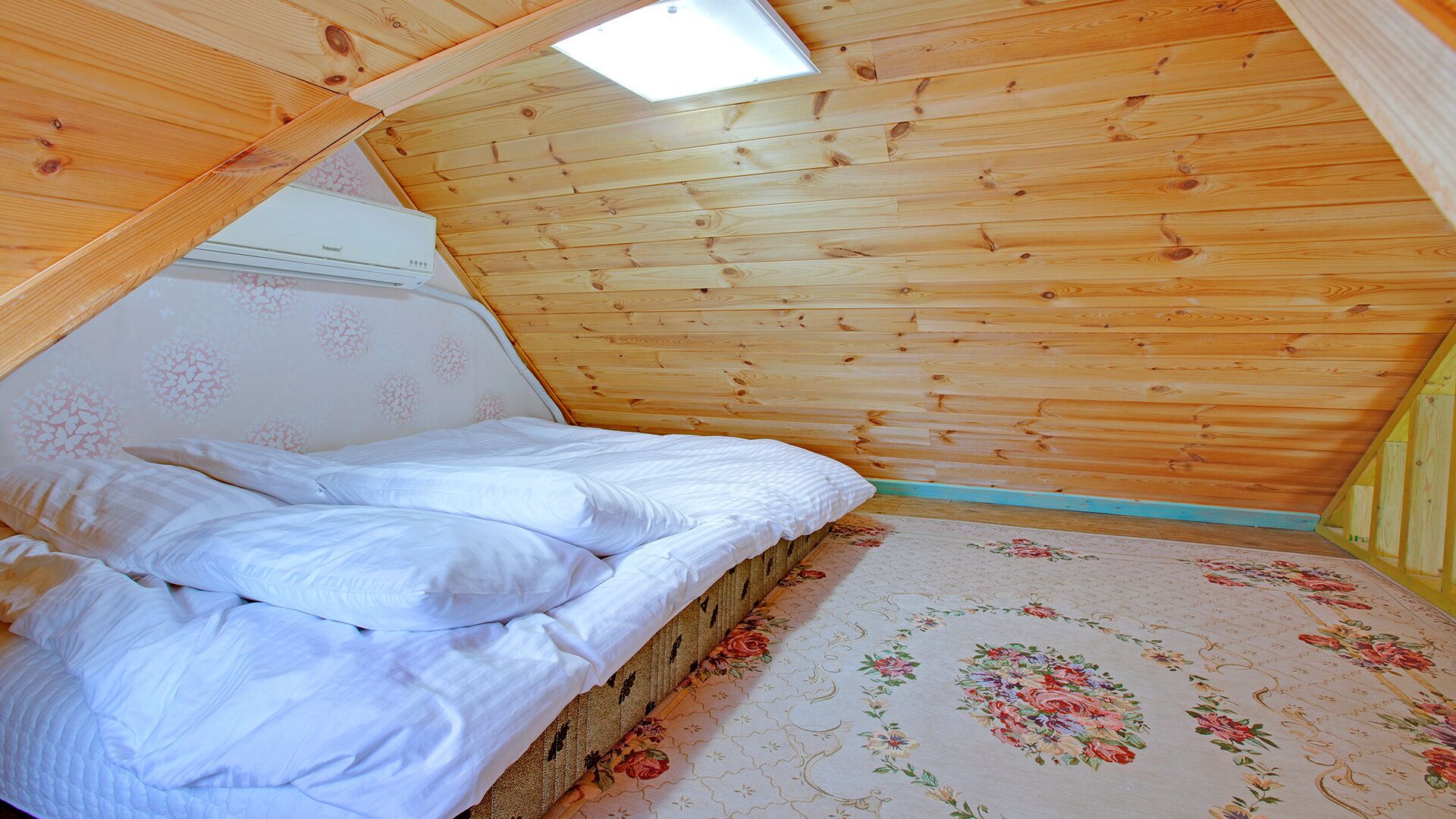 A small, cozy room with a sloped ceiling, a bed with white bedding, and a floral-patterned carpet.