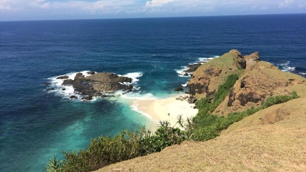 Un paisaje costero con una playa, afloramientos rocosos y aguas azules cristalinas.