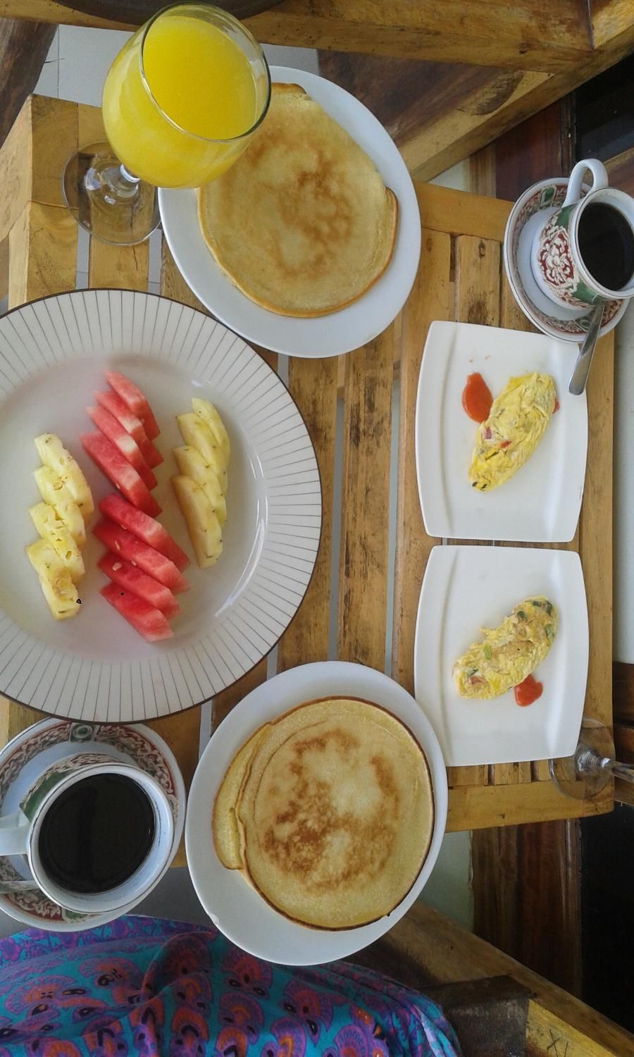 Une table de petit-déjeuner avec des crêpes, des œufs, des fruits et du café.