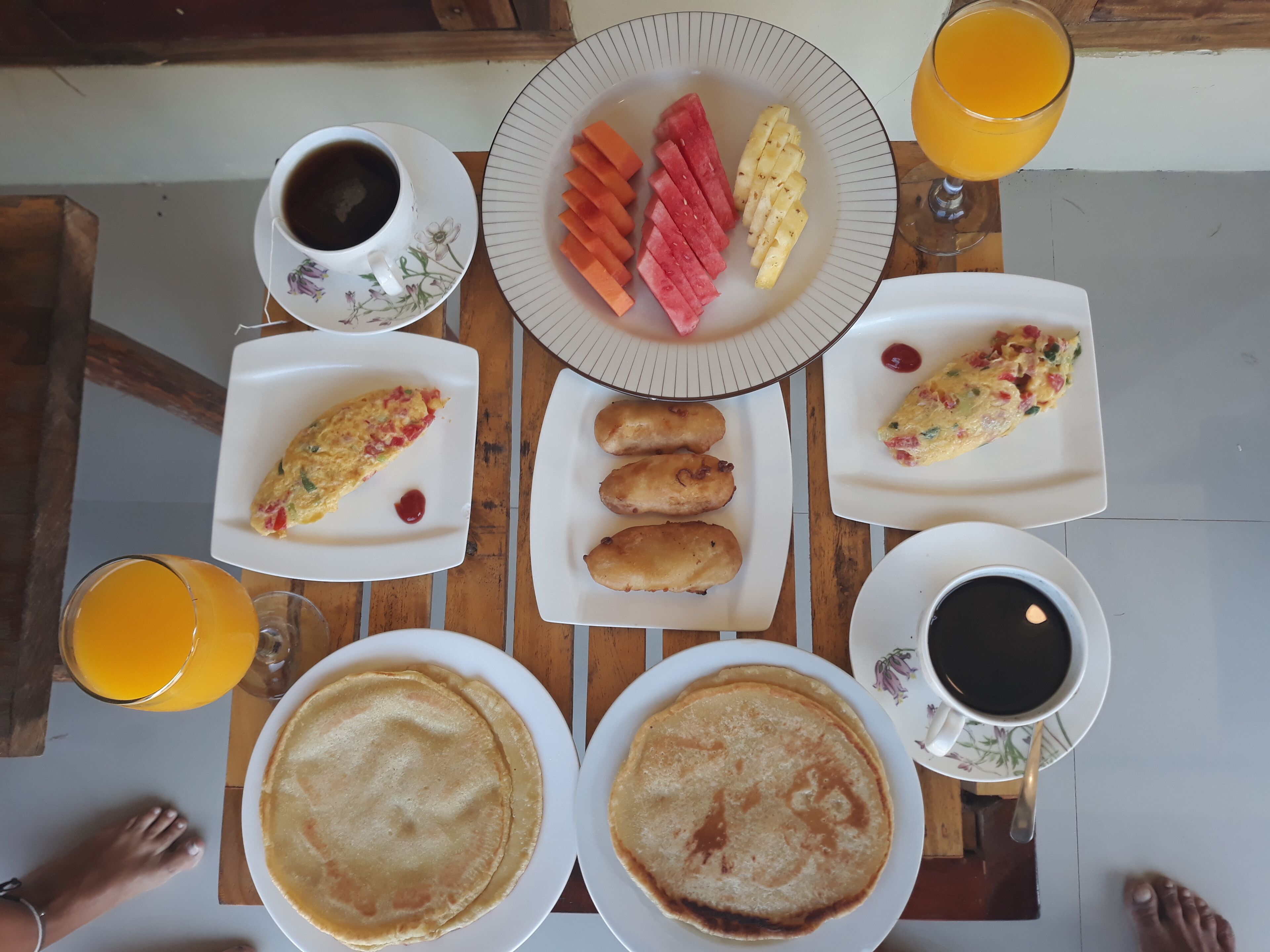 A breakfast table with plates of food, including omelets, pancakes, and fruit, along with cups of coffee and orange juice.