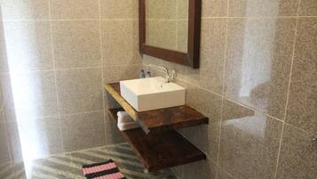 Un baño con un lavamanos blanco, encimera de madera y un espejo encima.