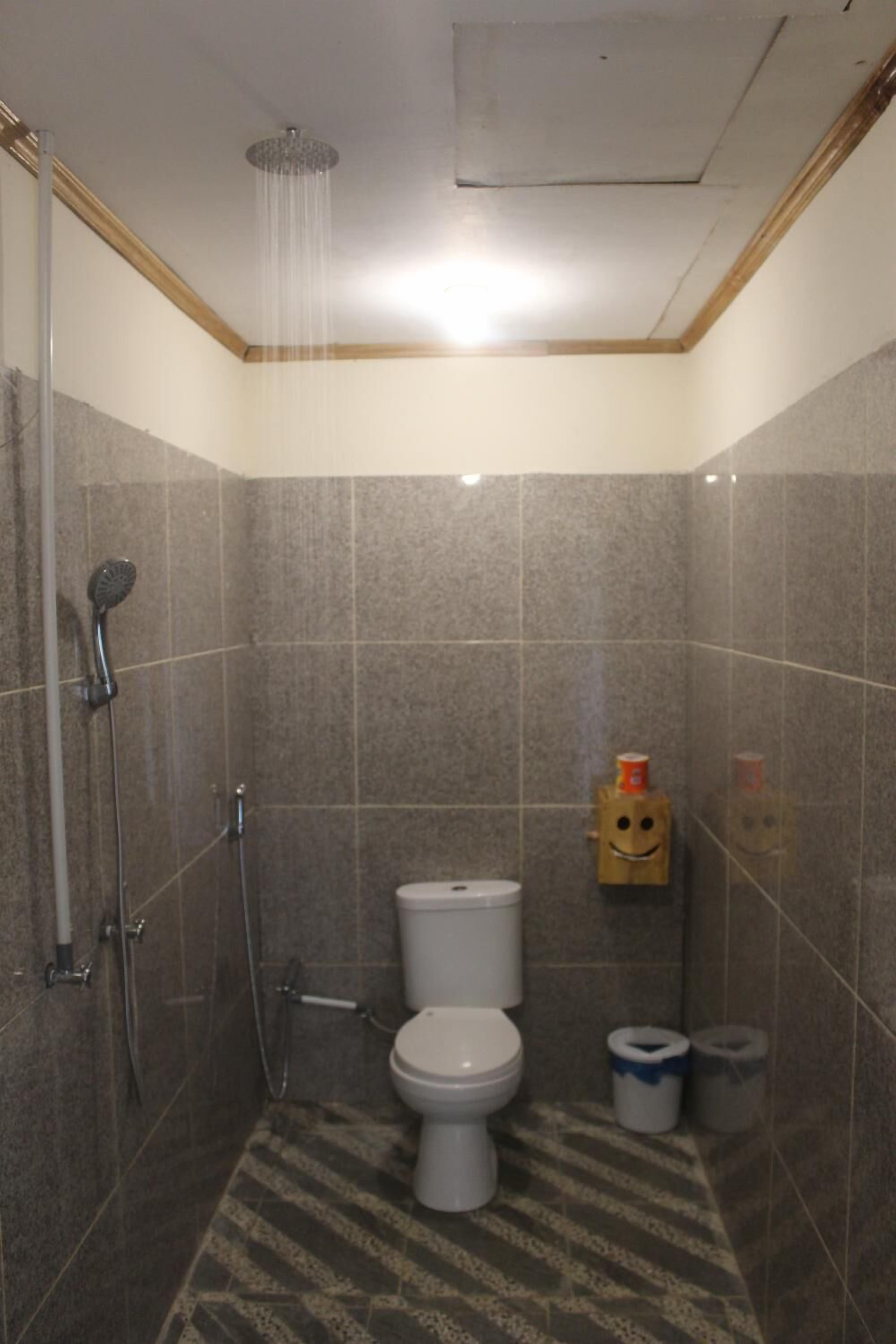 Een kleine betegelde badkamer met een douche, toilet en twee vuilnisbakken.