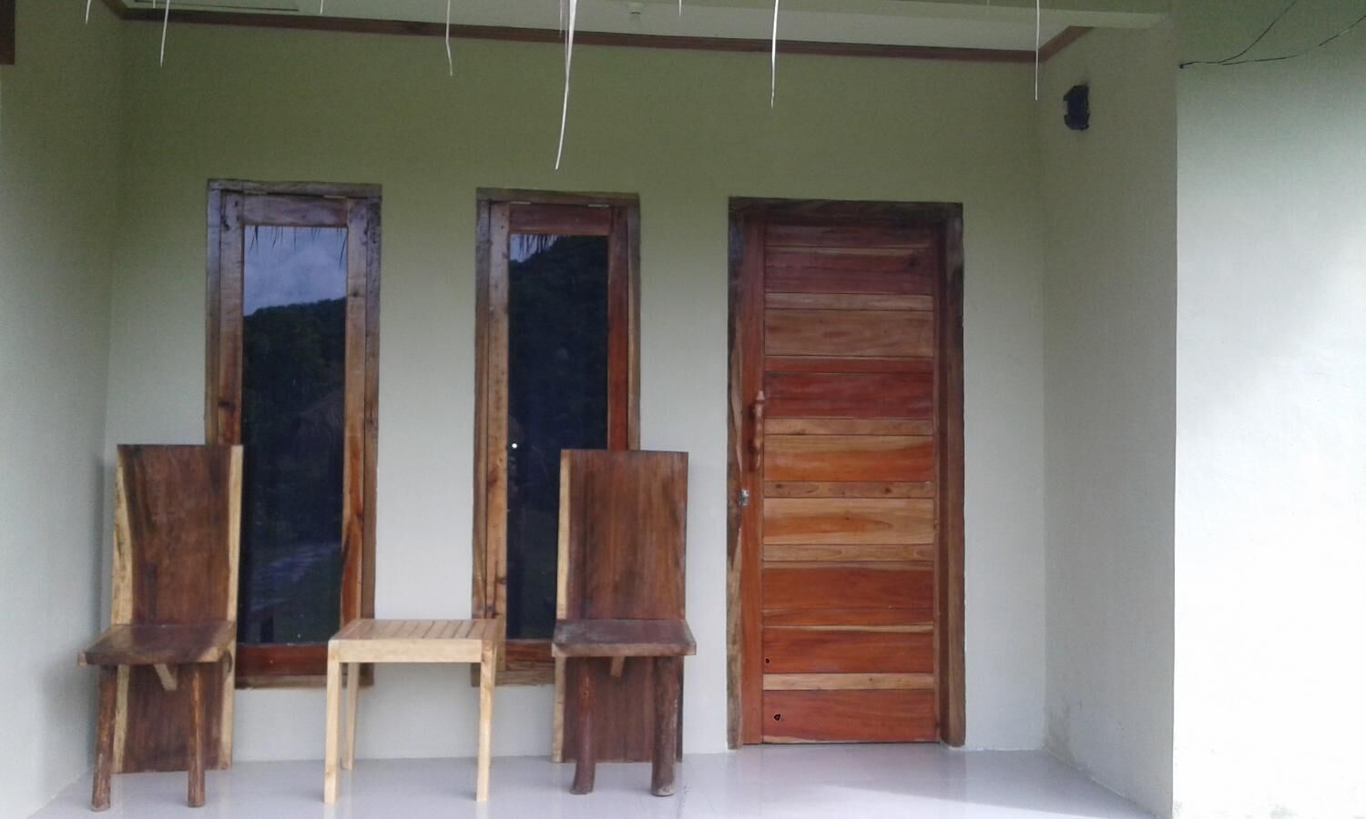 Un porche con dos sillas de madera y una mesita, una puerta de madera y dos ventanas.