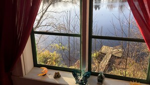 A window with a view of a lake and trees, curtains, and decorative items on the windowsill. - Tranquil Lakeside Cottage Retreat (Avesta)