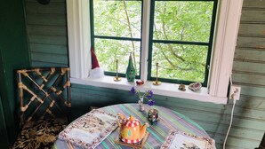 A room with a round table, a window with a view of trees, a chair, and a small shelf with decorative items. - Tranquil Lakeside Cottage Retreat (Avesta)