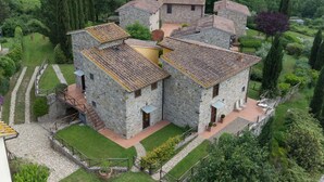A stone building with multiple rooms, surrounded by a well-maintained garden and a forested area. - Cosy apartment in villa for 7 guests with WIFI, pool, TV, patio and pets allowed (Greve In Chianti)