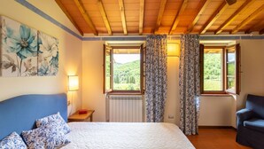 A bedroom with a bed, a chair, a radiator, and two windows with curtains. - Cosy apartment in villa for 7 guests with WIFI, pool, TV, patio and pets allowed (Greve In Chianti)