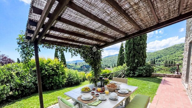 An outdoor dining area with a table set for breakfast, surrounded by lush greenery and a scenic view. - Cosy apartment in villa for 7 guests with WIFI, pool, TV, patio and pets allowed (Greve In Chianti)