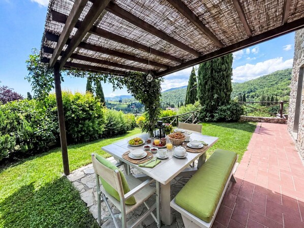Un espace de restauration en plein air avec une table dressée pour le petit-déjeuner, entouré d’une végétation luxuriante et offrant une vue pittoresque.