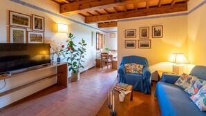 A living room with a television, sofa, and coffee table. There are framed pictures on the walls and a plant in the corner. - Cosy apartment in villa for 7 guests with WIFI, pool, TV, patio and pets allowed (Greve In Chianti)