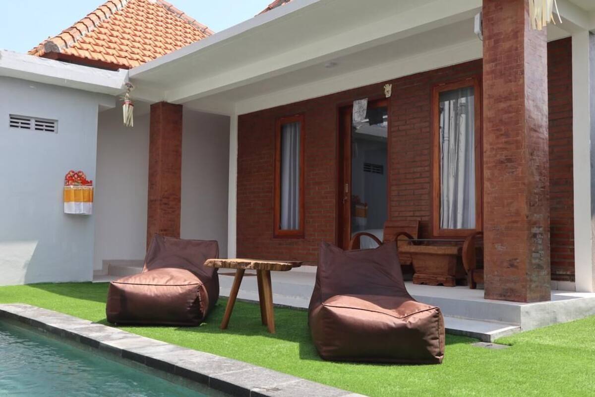 A poolside area with two bean bag chairs, a wooden table, and a brick wall.