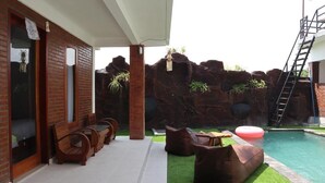 A pool area with a rock wall, lounge chairs, and a floating ring. - Gangga Guesthouse (Canggu)