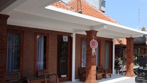 A traditional building with a tiled roof, wooden benches, and a decorative hanging ornament. - Gangga Guesthouse (Canggu)