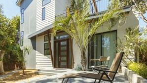 A modern two-story house with a balcony, a small garden, and a patio with outdoor furniture.