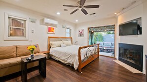 A bedroom with a bed, a sofa, a TV, a fireplace, and a ceiling fan.