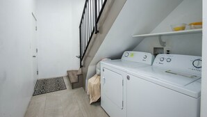A laundry room with a washing machine, dryer, and a small shelf with containers.