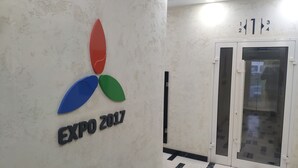 Eine Wand mit dem Logo der Expo 2017 und eine Tür mit beschrifteten Feldern.