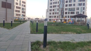 Ein Weg führt zu einem Spielplatz mit einem Pavillon, umgeben von Gras und Leitpfosten.