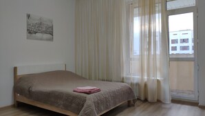 Ein Schlafzimmer mit Bett, einem Fenster mit transparenten Vorhängen und einem Stadtbild an der Wand.