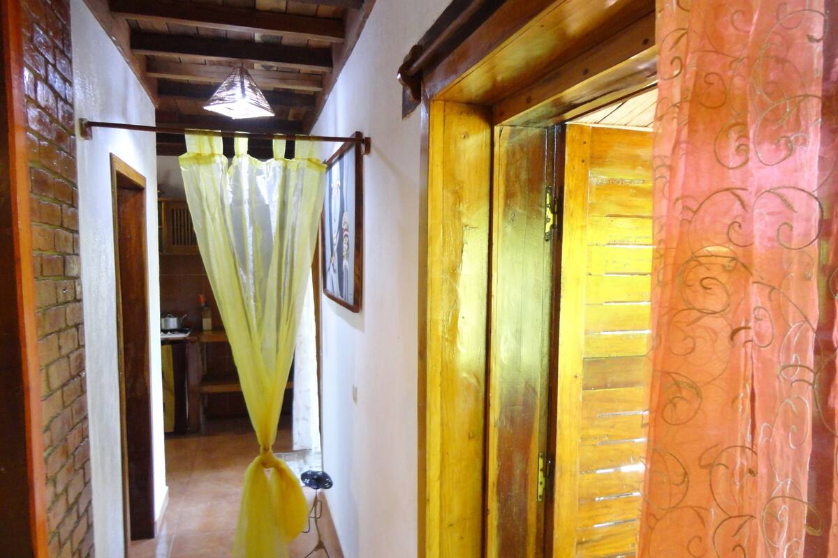 Un couloir étroit avec un plafond en bois, un rideau jaune et une porte ornée d’un rideau à motifs.