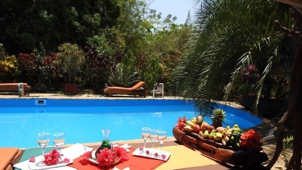 A poolside dining setup with a table set for two, featuring a fruit basket and wine glasses.