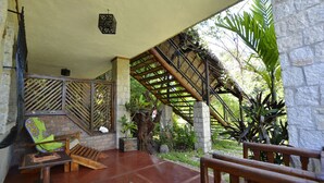 A covered outdoor area with a wooden bench, a table, and a staircase leading to a higher level.