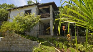 A two-story house with a stone facade, a balcony, and a garden with various plants.