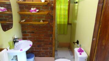 A bathroom with a brick wall, a white sink, a toilet with a leaf decoration, and a shower area with a green curtain.