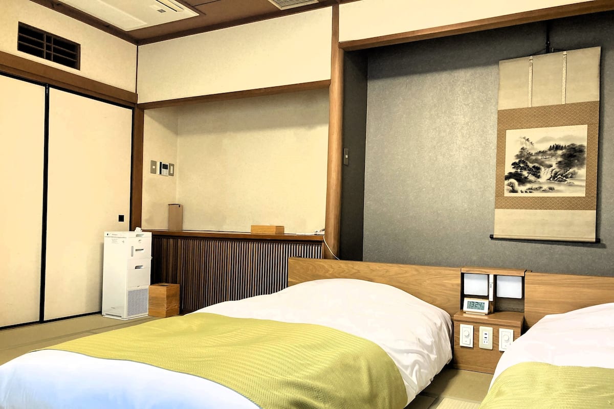 Une chambre d’hôtel avec deux lits, un petit bureau, une horloge murale et une œuvre d’art japonaise traditionnelle.