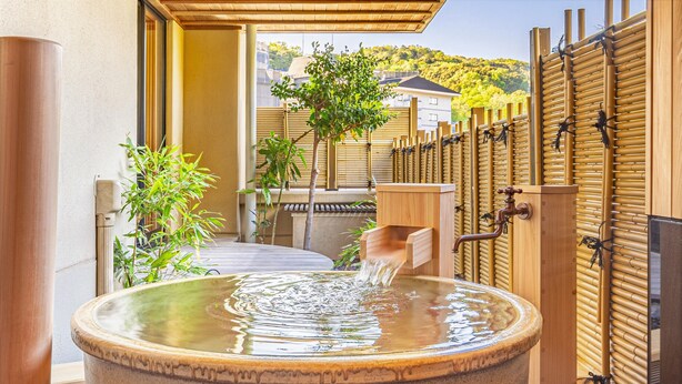 A stone hot spring bath with a wooden bench and a bamboo fence in the background.