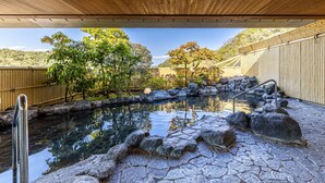 A stone pool with a wooden ceiling and bamboo walls, surrounded by rocks and trees.