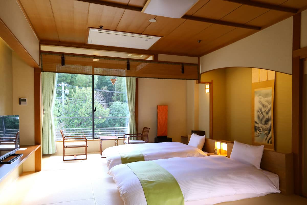 Une chambre d’hôtel avec deux lits, un bureau et une vue sur la verdure environnante.