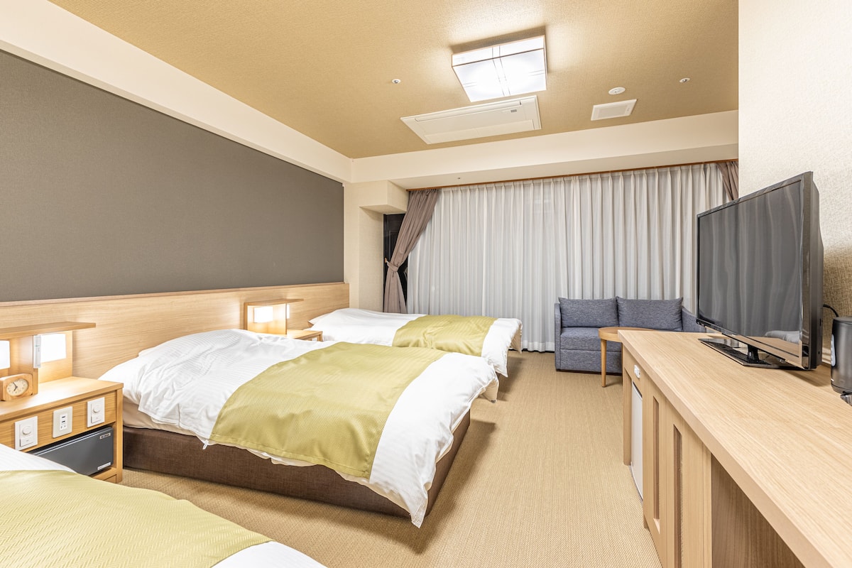 Une chambre d’hôtel avec deux lits, une télévision, un bureau et un canapé.