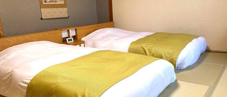 A hotel room with two beds, each with white linens and a green accent.