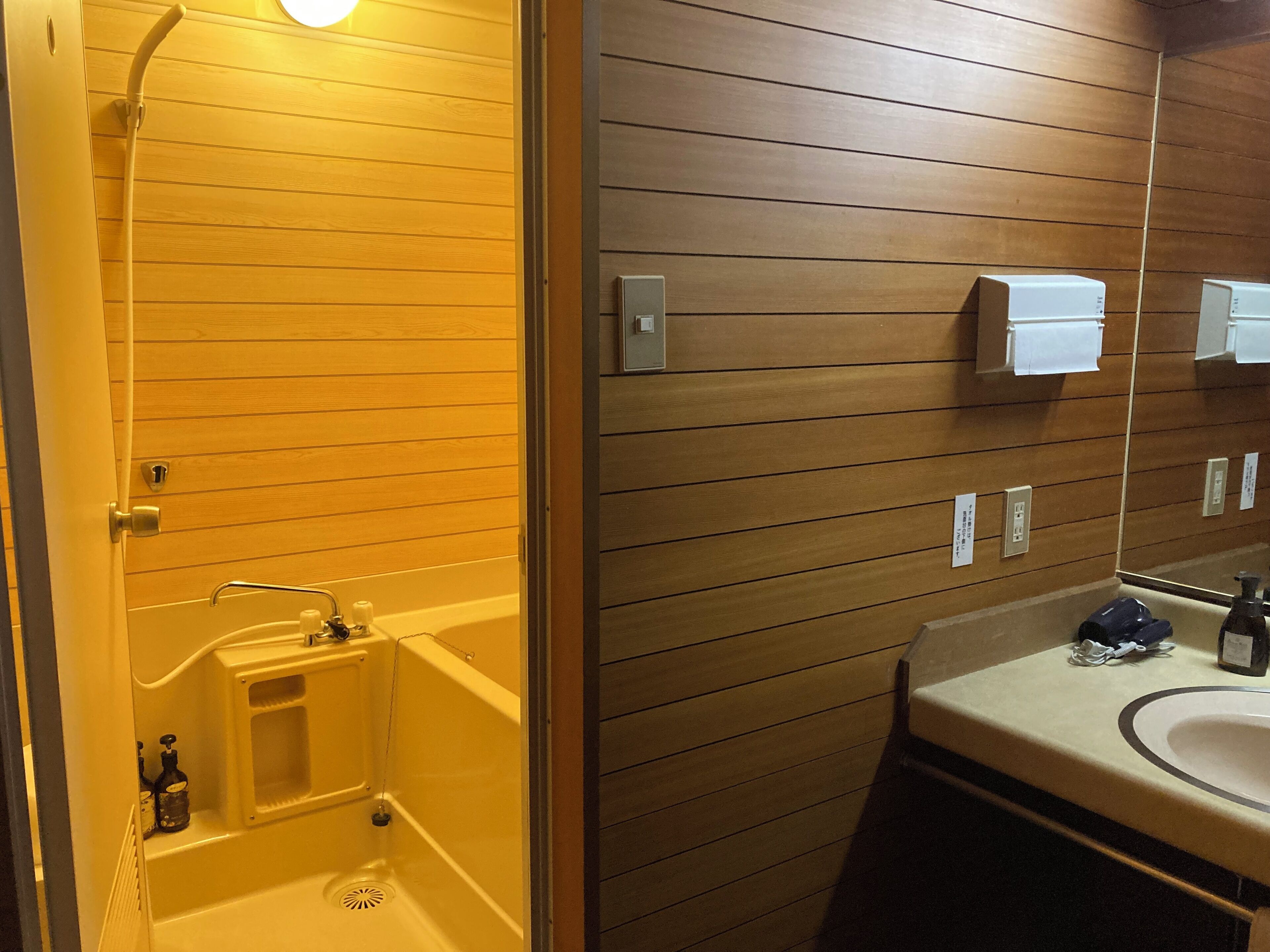 A bathroom with a wooden panel wall, a bathtub, a sink, and a mirror.