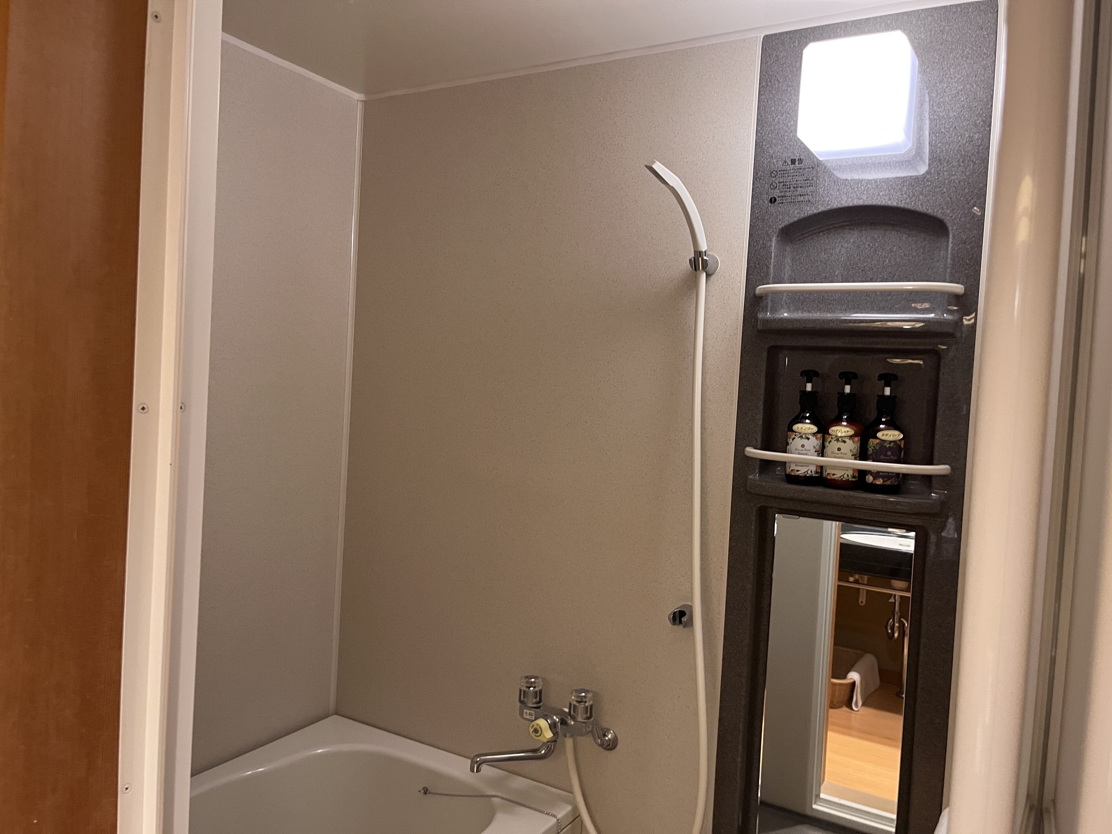 A bathroom with a bathtub, a shower, and a mirror. There are bottles on a shelf above the mirror.