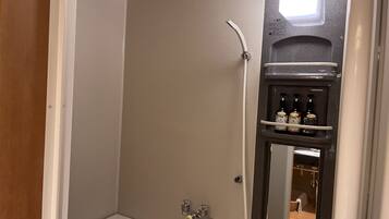 A bathroom with a bathtub, a shower, and a mirror. There are bottles on a shelf above the mirror.